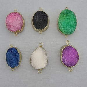 May include: Six gemstone pendants in various colors: pink, black, green, blue, white, and purple. Each pendant has a gold-colored metal frame and two small loops for attaching to jewelry. The gemstones have a textured, crystalline appearance.