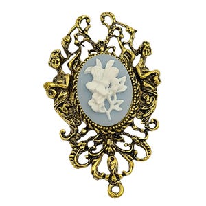 May include: A vintage-style brooch with a gold-tone filigree frame. The brooch features a pale blue oval cameo with a white floral design. Two sculpted figures flank the cameo, enhancing the antique aesthetic. A classic piece of jewellery.