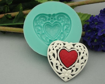 May include: A silicone mold for making a heart-shaped cake decoration. The mold is teal blue and the decoration is white with a red heart in the center.