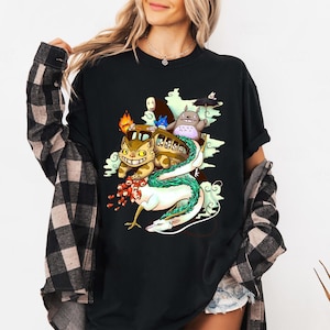 K&ouml;nnte beinhalten: Schwarzes T-Shirt mit einer farbenfrohen Grafik von Figuren aus einem beliebten Zeichentrickfilm. Das Design umfasst eine busf&ouml;rmige Katze, einen Drachen und andere skurrile Kreaturen. Das Shirt ist ein bequemer, l&auml;ssiger Stil.