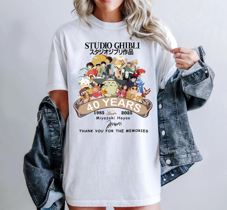 May include: White t-shirt featuring a colorful graphic of Studio Ghibli characters. The shirt commemorates 40 years with text that reads "STUDIO GHIBLI", "40 YEARS", and "THANK YOU FOR THE MEMORIES". The design includes Japanese text and the years 1985 and 2025.