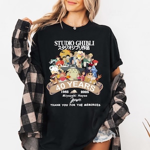 May include: Black t-shirt featuring a colorful graphic celebrating Studio Ghibli's 40th anniversary. The design includes characters from various Ghibli films, the text "STUDIO GHIBLI", and the years 1985-2025. The shirt also includes the text "THANK YOU FOR THE MEMORIES".