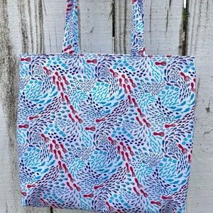 May include: A white tote bag with blue and red fish and squid patterns. The bag has two long straps.