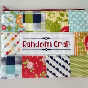 May include: A patchwork zippered pouch with a variety of fabric patterns, including floral, plaid, and polka dots. The pouch features the text "Random Crap" in red lettering on a white label. The zipper is burgundy.