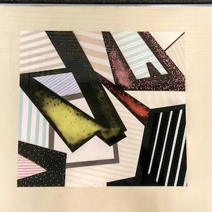Peut inclure: Impression d'art géométrique abstrait avec des rayures et des formes noires, blanches, grises, roses, bleues et jaunes. L'impression est encadrée dans un cadre noir.