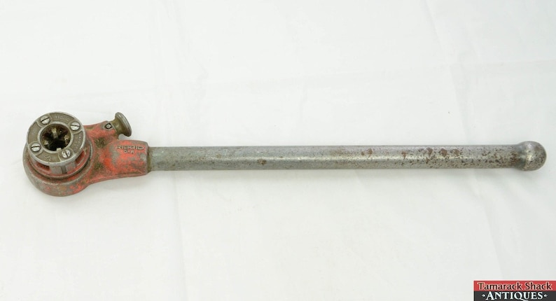 May include: A vintage red and silver pipe wrench with a long handle. The wrench has a round head with a gear mechanism and a knob for adjusting the size of the pipe.