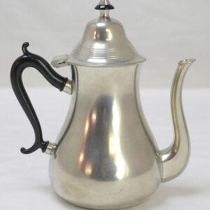 May include: A silver teapot with a black handle and a black knob on the lid. The teapot has a rounded body and a spout.