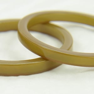May include: Two olive green plastic bangles. The bangles are smooth and shiny.