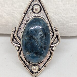 May include: A silver ring with a blue gemstone set in a diamond-shaped setting. The ring has a textured design and three silver accents.