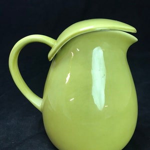 May include: A light green ceramic jug with a rounded body and a curved spout. The jug has a handle and a lid.