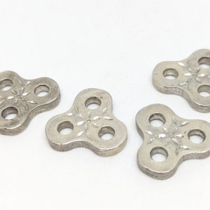 May include: Four silver-toned metal charms with three holes each. The charms are shaped like a three-leaf clover and have a decorative design in the center.