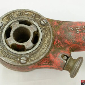 May include: A red and silver pipe wrench with the brand name "RIDDID" and the text "O-R" on the side. The wrench has a worn, rusty appearance.