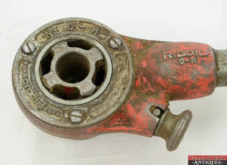 May include: A red and silver pipe wrench with the brand name "RIDDID" and the text "O-R" on the side. The wrench has a worn, rusty appearance.