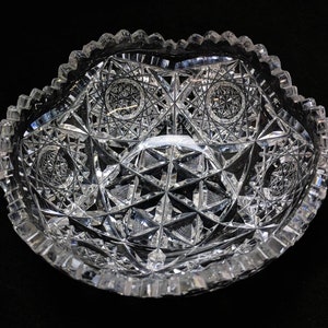 May include: A clear glass bowl with a scalloped edge and intricate cut glass design. The bowl has a starburst pattern and is perfect for serving fruit or snacks.