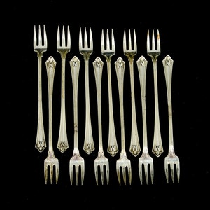 May include: Set of twelve silver-plated cocktail forks with a decorative design and the letter "M" engraved on the handle.