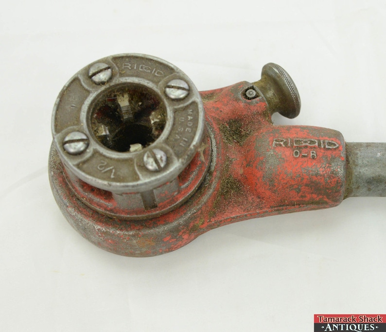 May include: A red and silver pipe threading tool with a 1/2 inch die. The tool is made in the USA and is labeled "RIDGID 0-R".