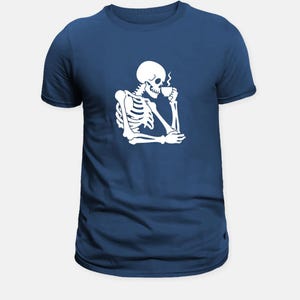 May include: Navy blue t-shirt with a white graphic of a skeleton enjoying a cup of coffee. The skeleton is shown in a relaxed pose, with steam rising from the cup. The design is simple and striking.