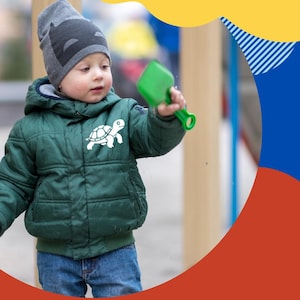 Puede incluir: Un niño pequeño con una chaqueta acolchada verde con un motivo de tortuga y un gorro gris, sosteniendo una pala de juguete verde. La imagen presenta el texto "Reflect with MOONFLECT" sobre un fondo colorido.
