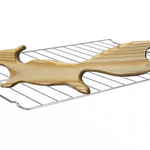 May include: A wooden squirrel-shaped cutting board with a handle featuring a circular hole. The board is light brown and rests on a chrome wire rack, set against a white background. This kitchen item is designed for food preparation.