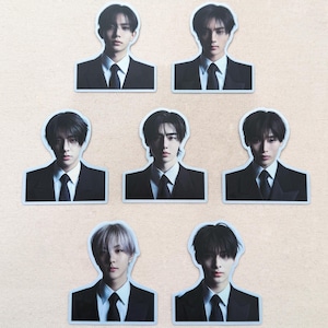 May include: Seven stickers featuring portraits of young men in black suits and ties. Each sticker has a white border. The men have various hairstyles and expressions. The stickers are arranged on a light beige surface.