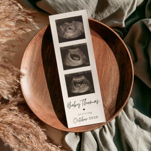 May include: A vertical white card featuring three black and white ultrasound images stacked vertically. Below the images, the text reads Baby Thomas, a small heart icon, the word arriving, and the date October 2026 in a black script and serif font.