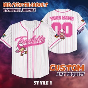 Könnte beinhalten: Weißes Baseball-Trikot mit rosa Nadelstreifen und Akzenten. Das Trikot zeigt den Namen "Toadette" in rosa Schrift auf der Vorderseite und eine Cartoon-Figur. Auf der Rückseite steht der Text "YOUR NAME" und die Nummer "00". Das Trikot ist für Kinder, Jugendliche und Erwachsene.
