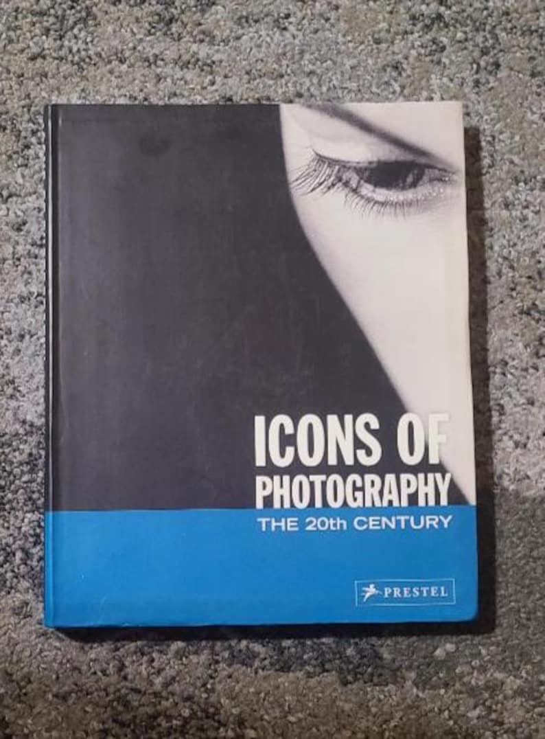 May include: A hardcover book titled "ICONS OF PHOTOGRAPHY THE 20TH CENTURY" with a black and white image of an eye on the cover. The book has a blue band at the bottom and the publisher's logo.