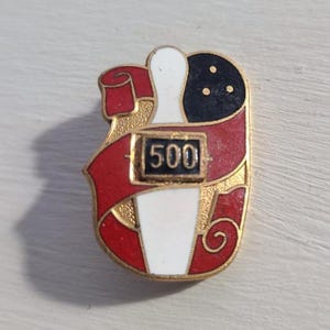 May include: A gold-tone bowling pin and ball pinback button with a red ribbon and the number 500 in a black rectangle.