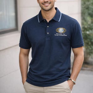 May include: A navy blue polo shirt with a white collar trim and the text "New York City Young Professionals" in gold and blue. The person is wearing khaki shorts.