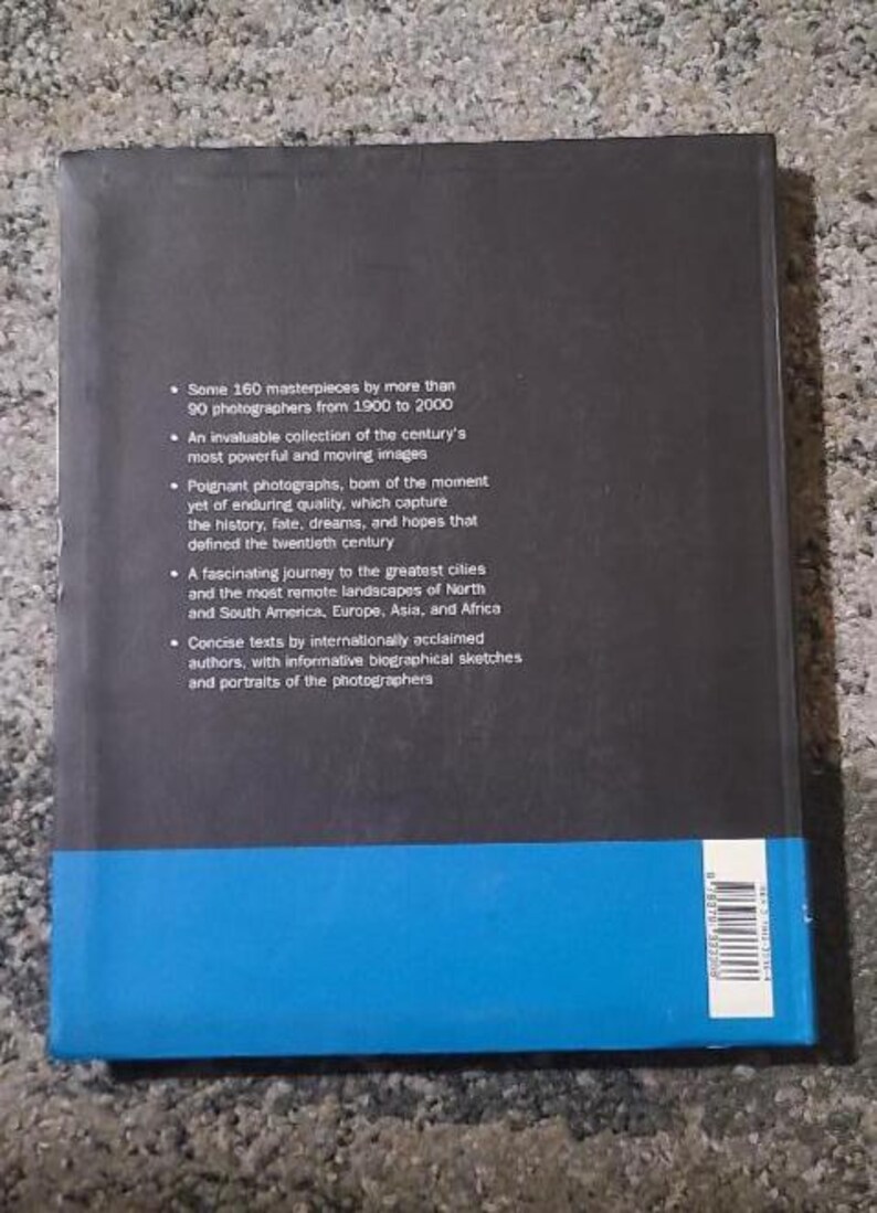 May include: A hardcover book with a black cover and a blue band at the bottom. The back of the book features text describing the contents, including 160 masterpieces by 90 photographers from 1900 to 2000.