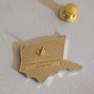 May include: A gold-colored pin in the shape of a flag, with a pin back and a separate gold-colored pin backing. The pin has the text "WWW.4PELPINSUNLIMITED.COM" and "1.888.888.PINS" on the back.