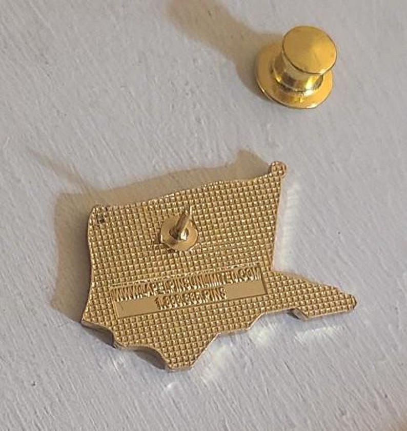 May include: A gold-colored pin in the shape of a flag, with a pin back and a separate gold-colored pin backing. The pin has the text "WWW.4PELPINSUNLIMITED.COM" and "1.888.888.PINS" on the back.