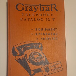 May include: An orange book with the title "Graybar Telephone Catalog 12-T" and a black and white illustration of a rotary dial phone. The text "Equipment, Apparatus, Supplies" is printed below the title. The book is labeled "Distributed by Graybar Electric Company."