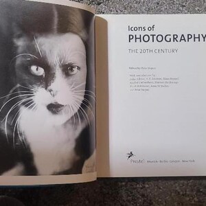 May include: A black and white photograph of a cat's face on the left page of a book. The right page displays the title "Icons of Photography: The 20th Century". The book is open, revealing the pages.