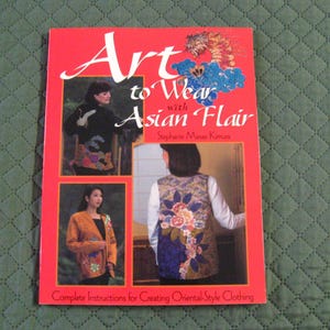 May include: Book cover with the title "Art to Wear with Asian Flair" by Stephanie Masae Kimura. The cover features three women wearing clothing with Asian-inspired designs. The book includes complete instructions for creating oriental-style clothing.