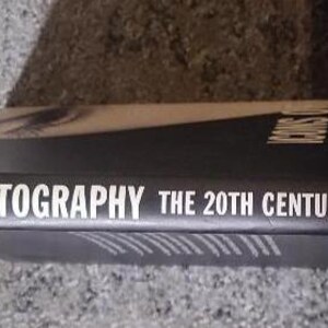 May include: A hardcover book titled "ICONS OF PHOTOGRAPHY THE 20TH CENTURY" with a black spine and blue cover. The title is in white font. The publisher's name, PRESTEL, is also visible.