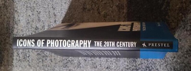 May include: A hardcover book titled "ICONS OF PHOTOGRAPHY THE 20TH CENTURY" with a black spine and blue cover. The title is in white font. The publisher's name, PRESTEL, is also visible.
