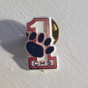 May include: White plastic pin with a red and blue outline. The pin features a large number "1" with a paw print inside. The bottom of the pin says "CHS" in black letters.