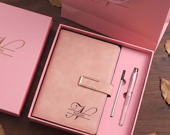 May include: A pink notebook with a gold-tone metal clasp and the name Natalie engraved in a script font, accompanied by a matching pink pen and a pen refill, all presented in a coordinated pink gift box and a matching pink paper gift bag.