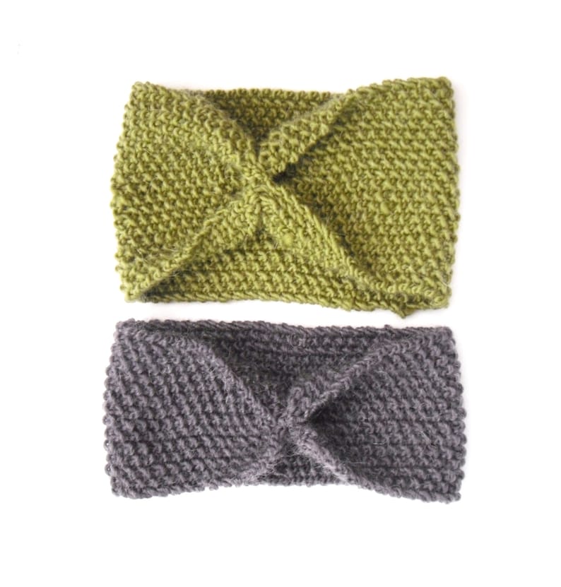 May include: Two knitted headbands. One is olive green, the other is gray. Both headbands have a twisted knot design in the center. The headbands are made of a thick, textured yarn and are displayed on a white background.