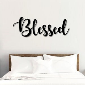 May include: A wooden bed frame with a white headboard and white bedding. The word "Blessed" is written in black cursive letters on the wall above the bed.