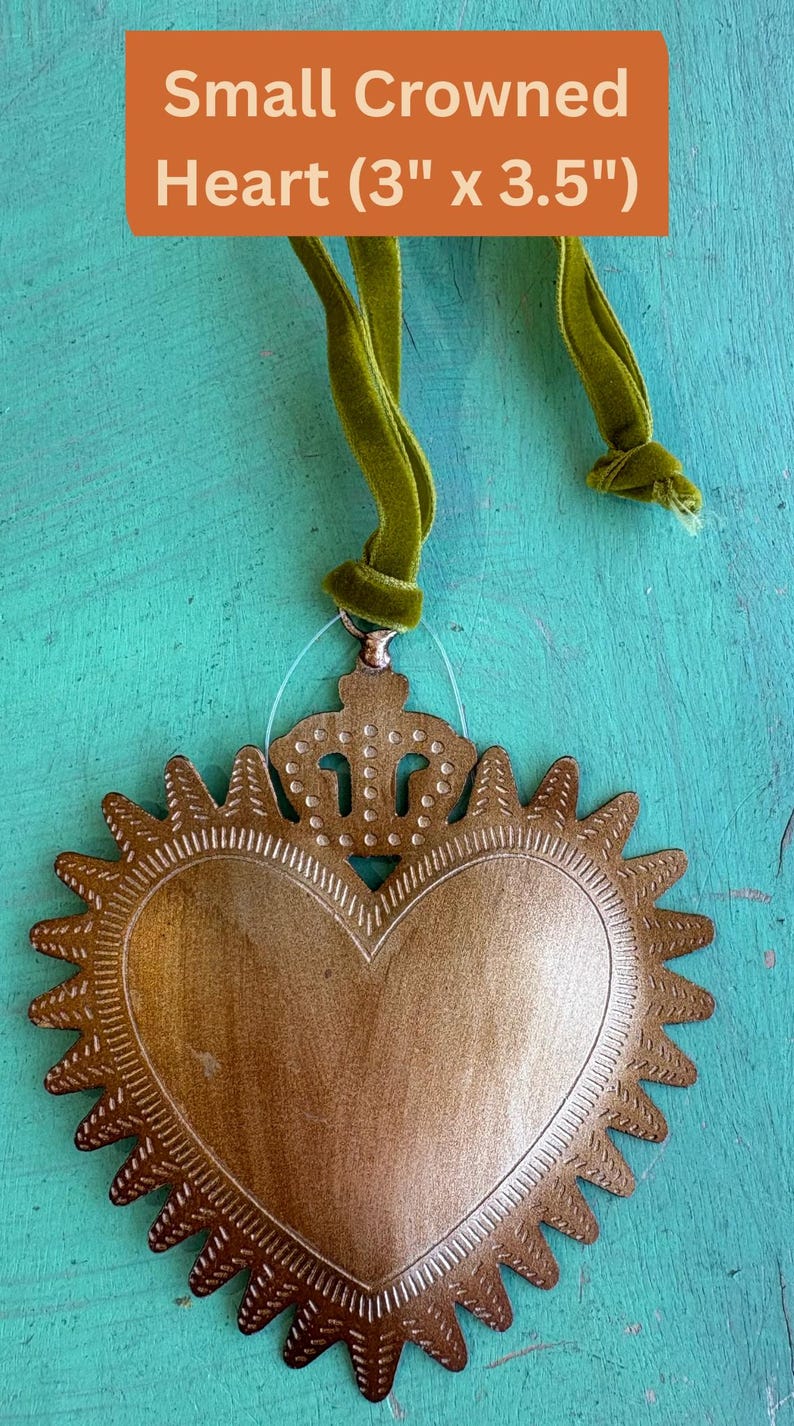 K&ouml;nnte beinhalten: Ein kleiner, goldfarbener Metallherzanh&auml;nger, 7,6 cm x 8,9 cm, mit Kronendetail und Sonnenstrahlenrand. Das Herz wird von einem gr&uuml;nen Samtband gehalten. Der Text "Small Crowned Heart (3" x 3.5")" befindet sich in einer orangefarbenen Box.