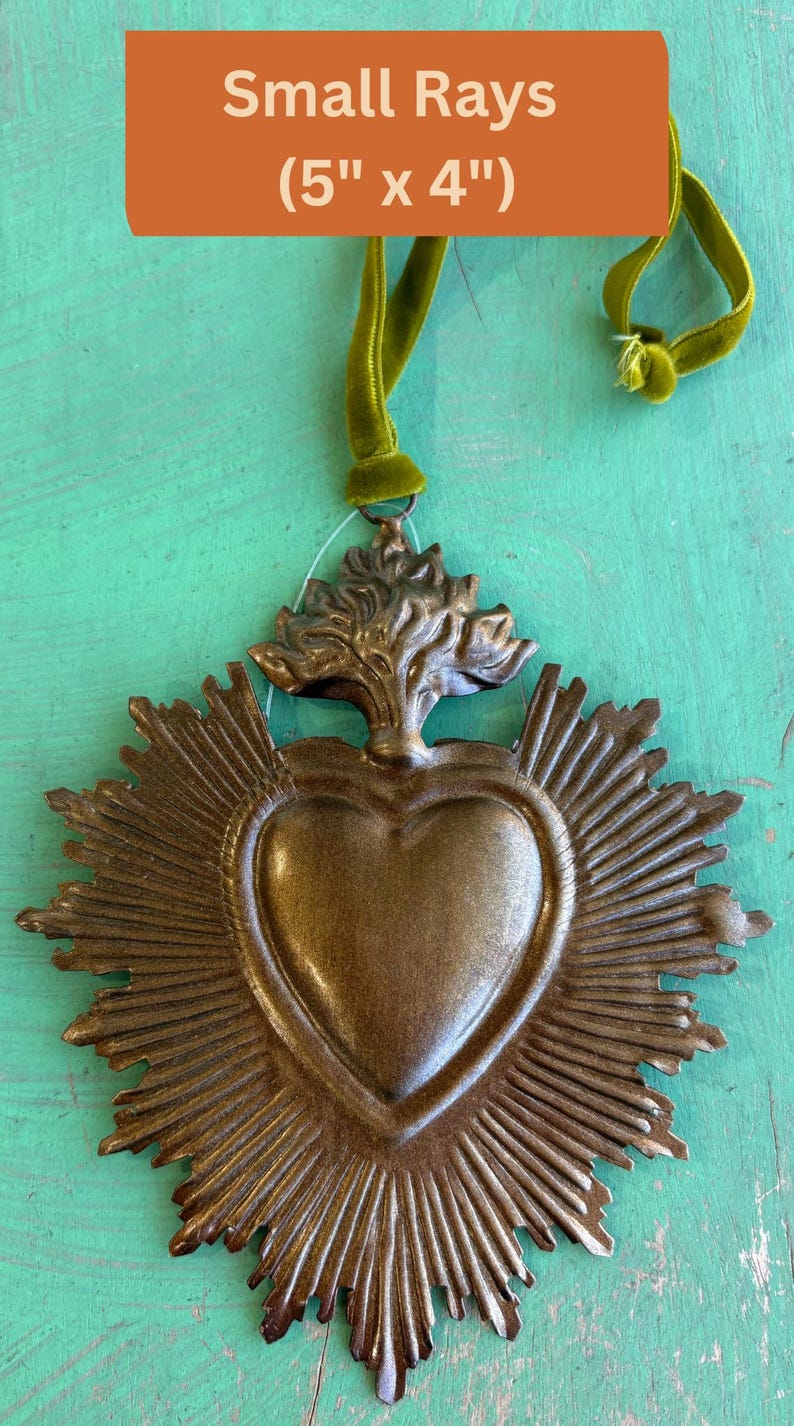 K&ouml;nnte beinhalten: Bronze-farbener Metall-Wandbehang in Herzform mit Sonnenstrahlen-Design, 12,7 cm x 10,2 cm. Das Herz ist mit einem baumartigen Design gekr&ouml;nt und hat ein gr&uuml;nes Samtband zum Aufh&auml;ngen. Der Text "Small Rays" befindet sich in einem orangefarbenen Rechteck.
