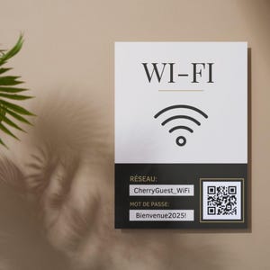 Peut inclure: Panneau Wi-Fi blanc avec texte noir et icône de signal. Le panneau indique le nom du réseau "CherryGuest_WiFi" et le mot de passe "Bienvenue2025!" ainsi qu'un code QR. Le fond est beige clair.