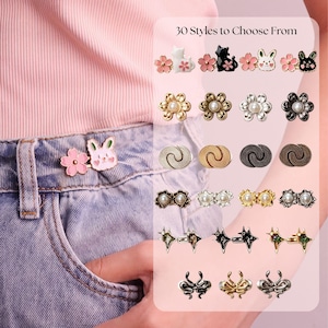May include: A set of metal waist tightening pins featuring 30 styles to choose from, including designs with cherry blossoms, rabbits, cats, pearls, stars, and abstract shapes. The pins are shown attached to light blue denim jeans and displayed in a grid.
