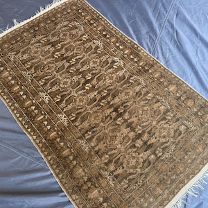 Könnte beinhalten: Rechteckiger brauner Teppich mit detailliertem, sich wiederholendem Muster. Der Teppich hat ein zentrales Design mit floralen und geometrischen Elementen, umrahmt von einem Rand. Die Kanten haben einen Fransenbesatz. Auf blauer Oberfläche.