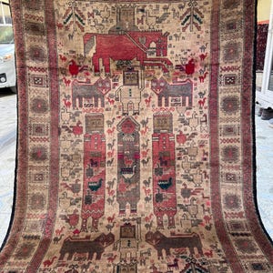 May include: A large, rectangular, vintage rug with a detailed, symmetrical design. The rug features a central field of beige and brown tones, with red and black borders. The pattern includes animal and geometric motifs, creating a traditional, decorative piece.