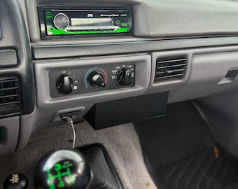 Puede incluir: Interior del salpicadero de un vehículo, con un sistema estéreo JVC y detalles en verde. Se ven mandos de control de clima y un compartimento de almacenamiento negro. También se aprecia un pomo de la palanca de cambios con marcas verdes y una palanca de cambios negra más pequeña.