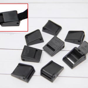 May include: Ten black plastic slide buckles. The buckles are rectangular with a small hole on one side and a larger hole on the other. The buckles are designed to be used with webbing or straps.