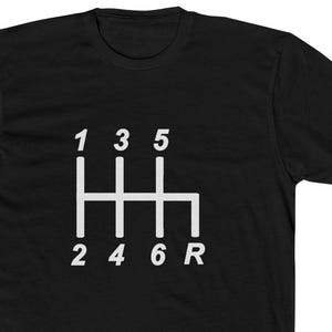 Puede incluir: Camiseta negra con un gráfico blanco del patrón de cambio de marchas de un coche. Se muestran los números 1, 3, 5, 2, 4, 6 y R. La camiseta está hecha de un material suave y cómodo.
